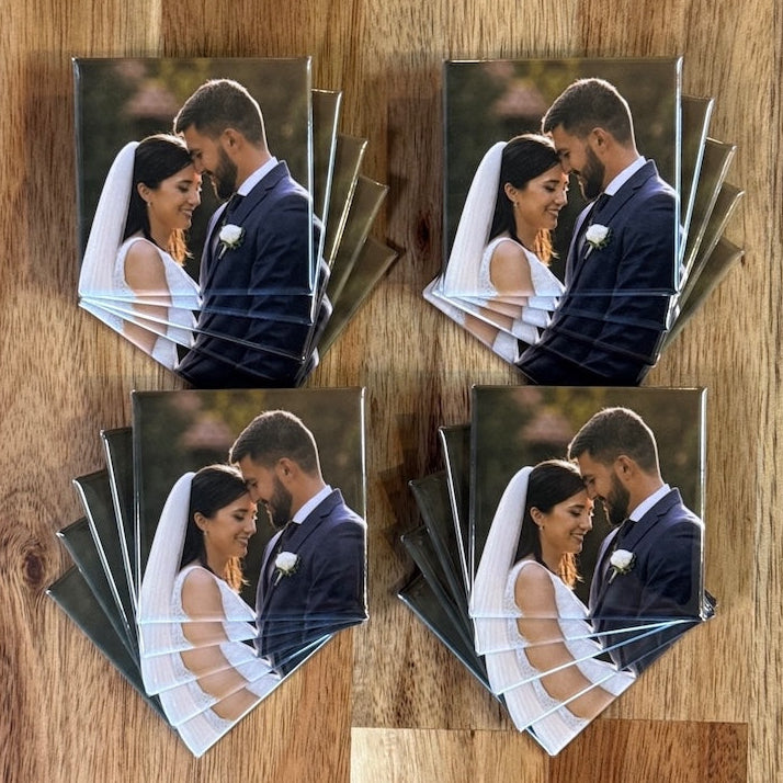 Twenty identical square photo magnets of a wedding couple, fanned in four stacks on a wood table, made as wedding favors
