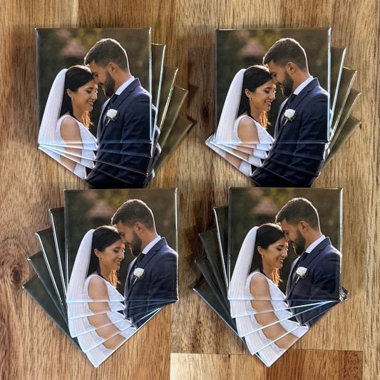 Twenty identical square photo magnets of a wedding couple, fanned in four stacks on a wood table, made as wedding favors