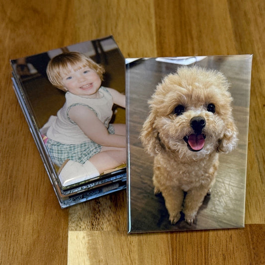 Nine 2×3 inch rectangle photo magnets stacked on a wooden table, with one showing a tan poodle and another a vintage photo of a young girl